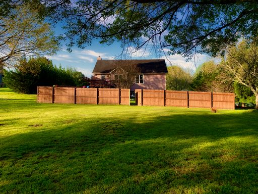 A beautiful view of a wooden house with a backyard and fence in the countryside on a sunny day