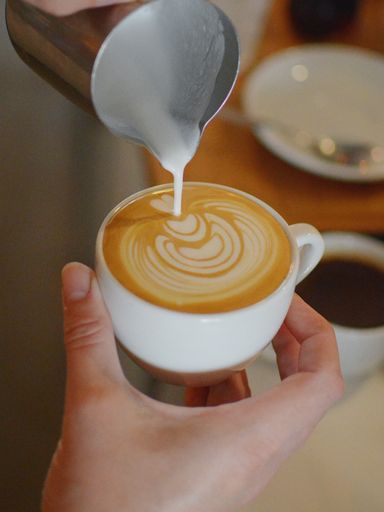 A vertical closeup shot of a female barista pouring stream milk into the coffee for making latte