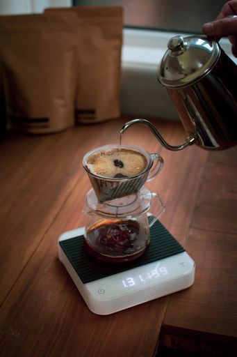 A vertical shot of a male pouring boiled water into the pour over coffee maker