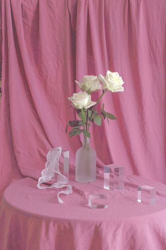 A vertical shot of white roses with beautiful glass bottles on a pink fabric surface and background
