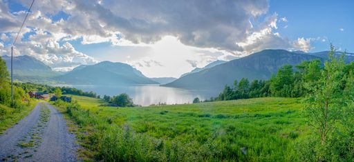 A beautiful view of a road surrounded by green fields and mountains under a cloudy sky