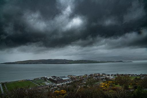 A scenic view of the seashore by the tranquil water under the stormy sky