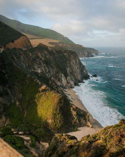 A vertical high angle shot of the ocean waves hitting the coast with cliffs