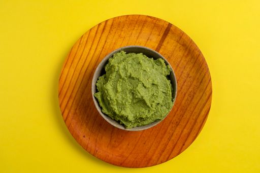 A top view of smashed avocado in a small ball isolated on a wooden plate on a yellow background