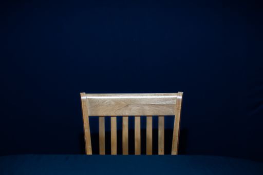 A single wooden chair in front of a table on a dark blue background