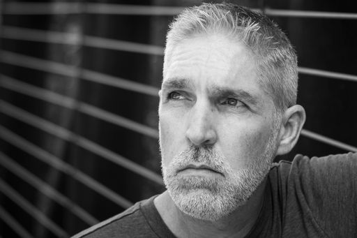 A grayscale shot of a male Caucasian leaning against the grilled fence