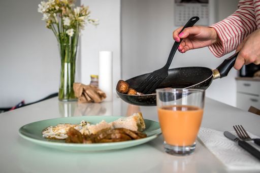 Picture of Vegan Meatballs Being Served from the Pan by Women's Hands on a Plate with Bread, Tomato Slices and a Glass of Creamed Salmorejo