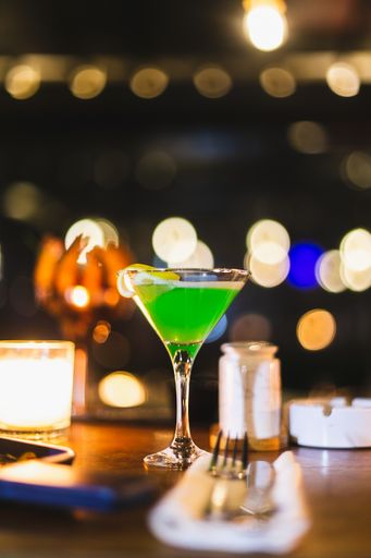 A vertical shot of a green cocktail in a martini glass on a bokeh background