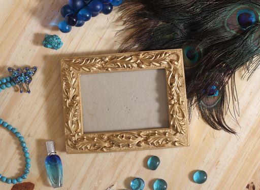A blue jewelry and peacock feathers with an ampty gold picture frame on a wooden background
