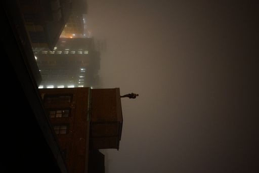 A vertical view of the silhouette of a man standing on a building in the dark