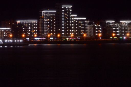A wide shot of high buildings with lights reflected in the water under the beautiful night sky