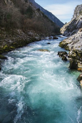 A vertical shot of a beautiful wild river streaming through rocks in between mountains