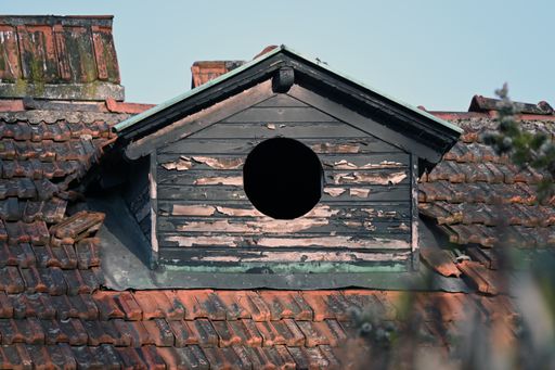 An old house roof with chipped paint and a round window with the sunlight shining on it