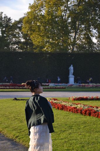 A vertical shot of an Asian girl admiring Schloss Schonbrunn from its garden, Vienna, Austria
