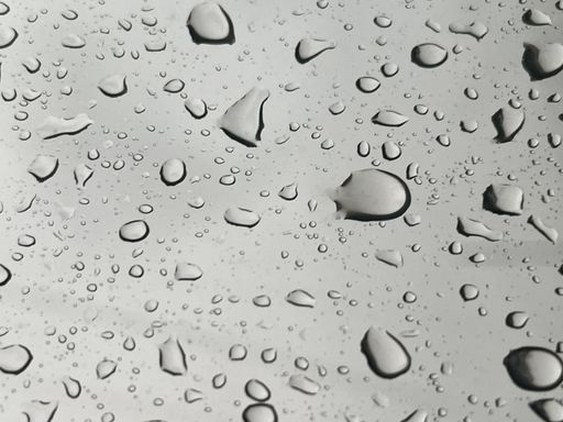 A vertical shot of raindrops running down a window on a grey background