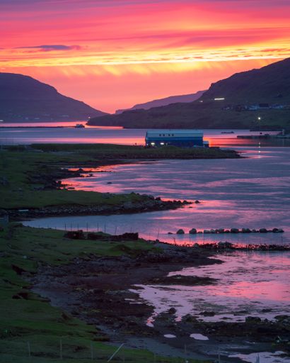 A vertical shot of a body of water near the shore with a dramatic colorful sky in the background