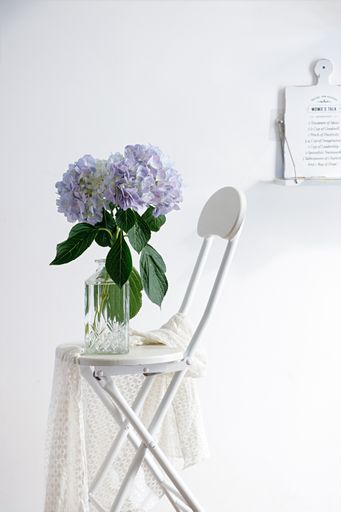 The vertical studio shot of still life composition with a white chair and a vase with purple flowers