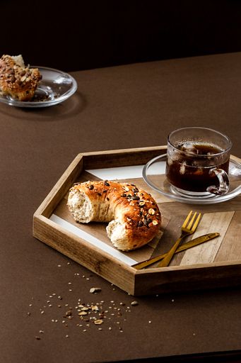 A closeup shot of a cup of tea and fresh bread bagel roll with seeds on a table