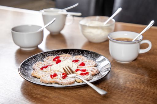 A selective of a table with a fresh waffle on a black plate with wooden background and a coffee cup