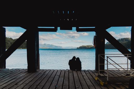 The silhouette of the couple sitting on the dock against the background of the sea and mountains.