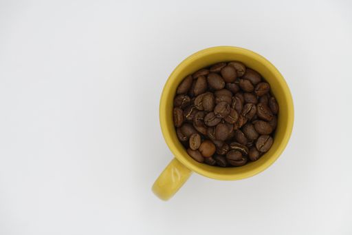 A high angle shot of coffee beans in a yellow cup on a white background
