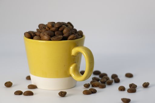 A high angle shot of a cup of coffee beans with some beans spilled on a white surface