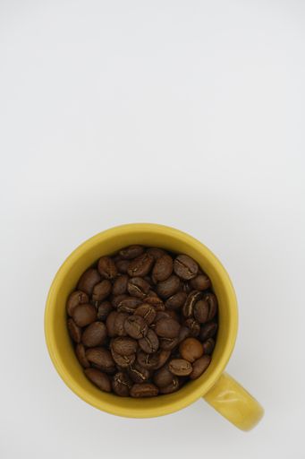 A high angle shot of coffee beans in a yellow cup on a white background