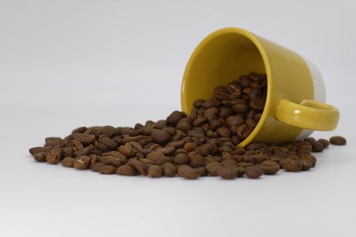 A high angle shot of a cup of coffee beans with some beans spilled on a white surface