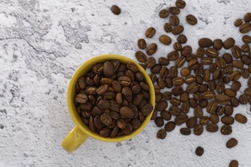 A high angle shot of a cup of coffee beans with some beans spilled on a white surface