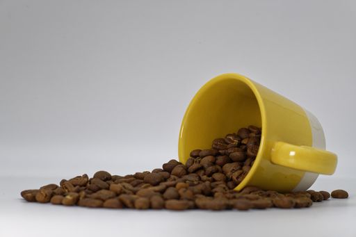 A high angle shot of a cup of coffee beans with some beans spilled on a white surface
