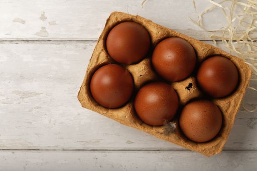 A high angle shot of a box of red eggs on s wooden surface