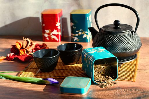 A teapot with loose green tea leaves with cups and bamboo mat