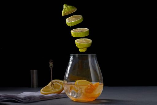 A jar of lemonade and sliced green lemon in the air cut out against a black background