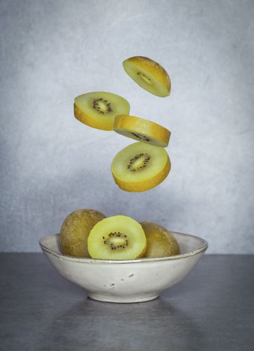 A vertical shot of kiwi slices falling into a white plate