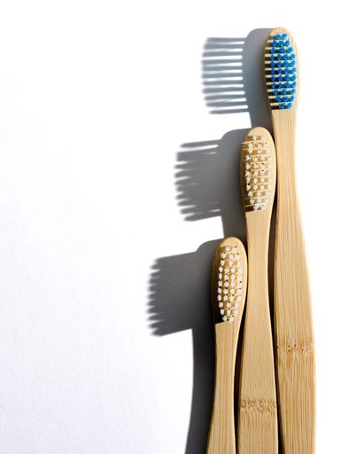 A photo of eco-friendly bamboo toothbrushes with white and blue bristles on a white background