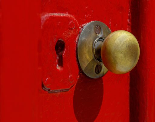 A closeup shot of an old style door handle and keyhole on a red a door in bright sunlight