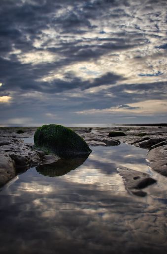 A vertical shot of a body of water in a rocky shore under a dramatic cloudy sky