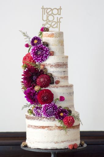 A vertical shot of a large 4 tier cake with colorful fresh flowers on a white background