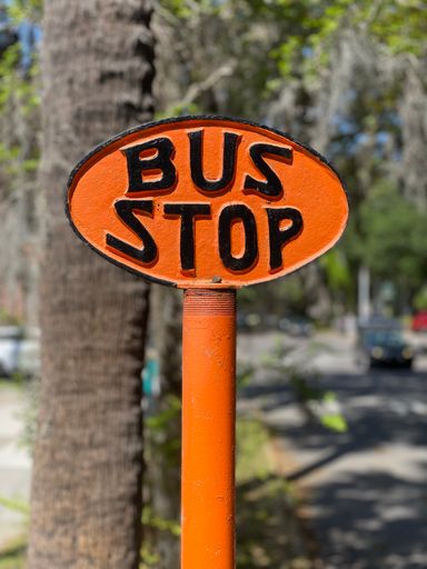 A vertical shot of an orange round bus stop sign with black letters