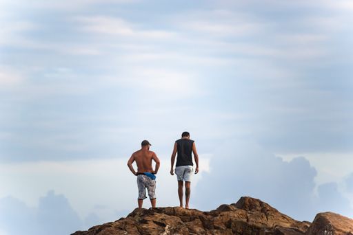 Two men standing on a big rock at Farol da Barra beach in Salvador city, Bahia, Brazil