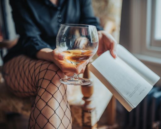 A sexy woman wearing fishnet stockings holding a glass of whiskey and a book