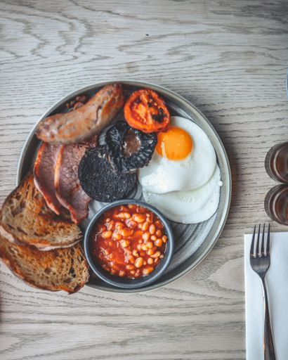 A top view of fried eggs, sausage, toast, onions, and tomatoes with a bowl of beans in red sauce