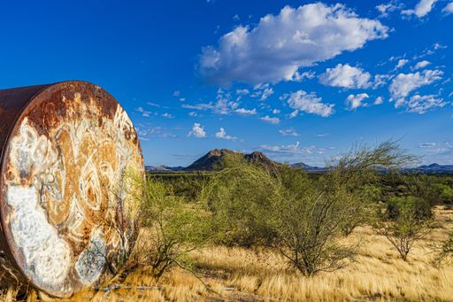The image shows the desert landscape with a large metal tank left by the trail and vandalized with grafiti