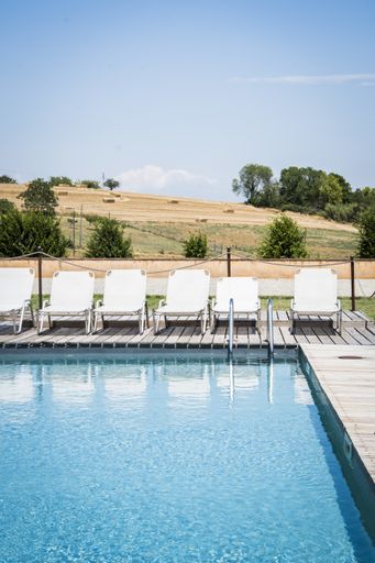 A vertical shot of a swimming pool with six white deck chairs near the pool during the daytime