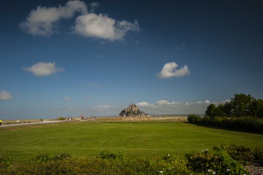 A beautiful landscape shot of a green field with the Mont Saint Michel in the background on a cloudy day in Normandy, France