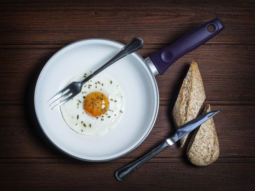 An overhead shot of a sunny side up egg in a pan near a sliced bread on a wooden surface