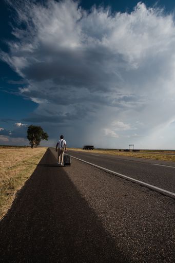 A man walking on the road with his suitcase under the cloudy and rainy sky