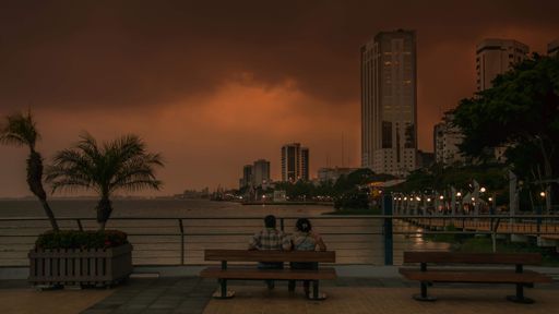 A scenery of sunset in the city with a couple sitting on a bench at the pier