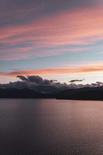 A vertical shot of a aesthetic cloudy orange sunset over mountains and a lake