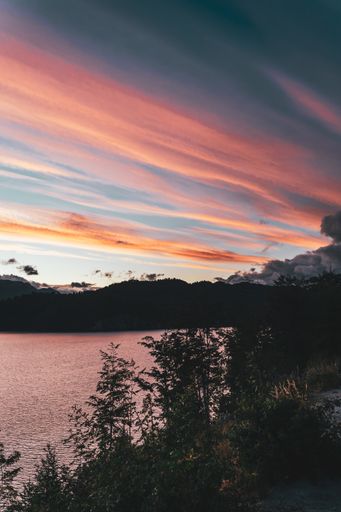 A vertical shot of a aesthetic cloudy orange sunset over mountains and a lake